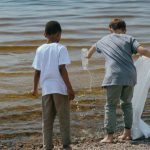 Ocean Cleaning - Young Boys Holding a Sack and Plastic Bottle Standing on Seashore