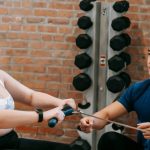 Training Workout - Multiethnic trainer and overweight woman doing exercises with rowing machine together in sport club