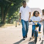 Family Time - Man Standing Beside His Wife Teaching Their Child How to Ride Bicycle