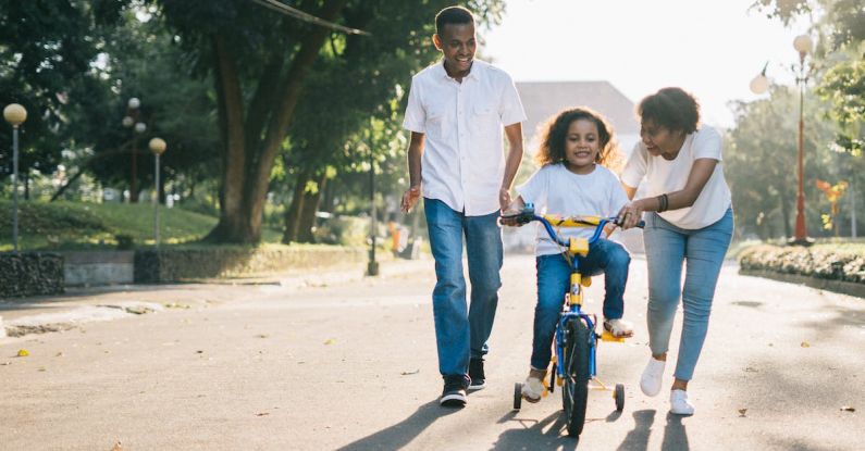 Family Time - Man Standing Beside His Wife Teaching Their Child How to Ride Bicycle