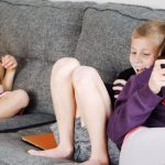 Positive Habits - Positive barefoot children in casual wear resting together on cozy couch and browsing tablets and smartphones