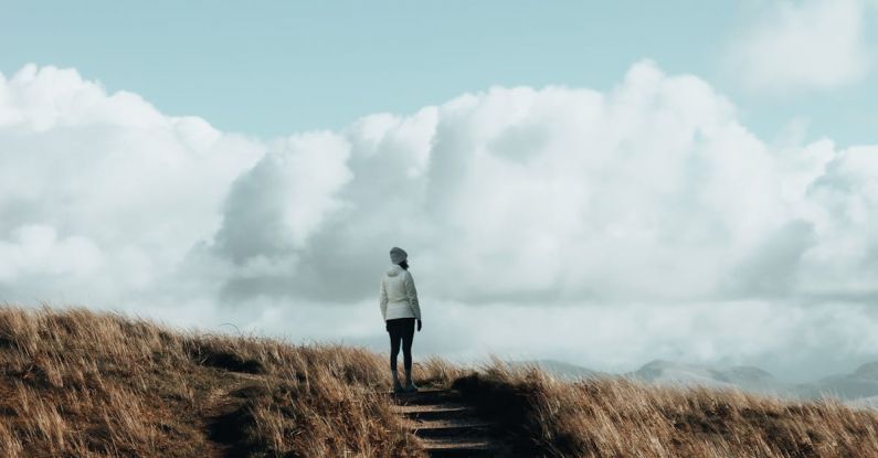 Hiking Adventure - A person walking up a hill with clouds in the sky