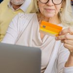 Family Budget - Elderly Couple Sitting on Blue Sofa and Looking at Bank Card