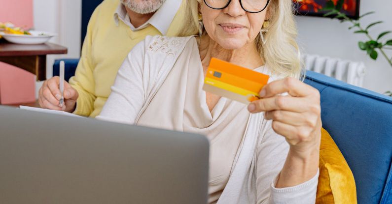 Family Budget - Elderly Couple Sitting on Blue Sofa and Looking at Bank Card