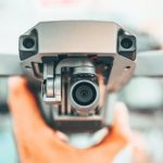 Drones Use - Crop unrecognizable person holding contemporary drone against blurred interior and demonstrating powerful camera