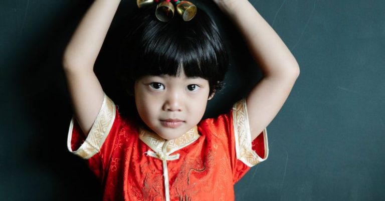 Feng Shui - Calm Asian child holding New Year toy above head and looking at camera