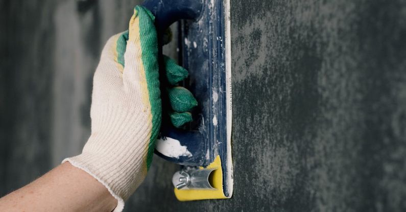 Home Repair Tools - Crop anonymous male worker in gloves holding scraper and aligning walls in flat
