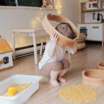 Gluten-free Pasta - Full length of anonymous toddler squatting barefoot on floor playing with round wooden shapes of different size and pasta and putting biggest shape on while developing fine motor skills at home